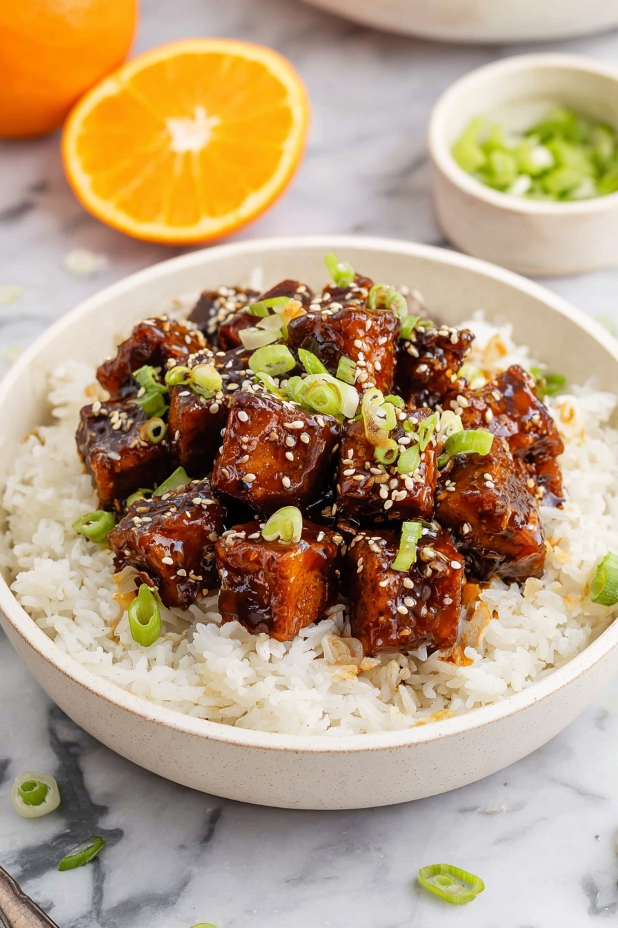 A white bowl filled with a base layer of fluffy white rice, topped with a layer of glossy, dark brown cubes of tofu coated in a shiny sauce. The tofu layer is sprinkled with small white sesame seeds and thinly sliced green onions, adding a fresh green color contrast. The bowl is placed on a white marbled surface, and there is a halved orange in the background along with a small white bowl of green onion slices. photo taken with an iphone --ar 2:3 --v 7