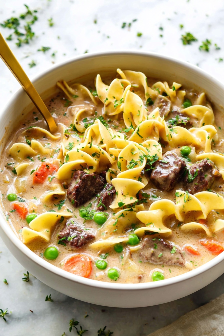 The image shows a white bowl filled with creamy beef and noodle soup. The soup has three main layers: the first is a thick, beige liquid base, the second consists of egg noodles that are pale yellow with a smooth, twisted texture, and the third layer includes dark brown chunks of beef, bright green peas, and small orange carrot pieces scattered throughout. The soup is topped with finely chopped fresh green herbs, adding a touch of color and freshness. A gold spoon rests inside the bowl, and the bowl is placed on a white marbled surface with some herbs sprinkled around. photo taken with an iphone --ar 2:3 --v 7