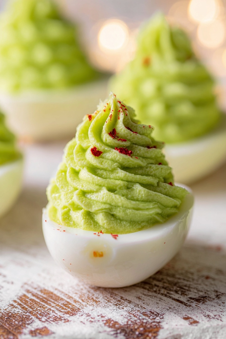 The image shows several pieces of halved hard-boiled eggs with smooth white bases, each topped with a tall, spiral swirl of light green creamy filling that looks soft and slightly textured. The green filling is sprinkled with small red and black spice flakes for decoration. One of the egg halves in the center has a bright yellow star-shaped slice placed on top of the green swirl, adding a pop of color. The eggs are placed on a white marbled surface with some shadow and light reflections. The background is blurred, making the eggs the clear focus of the image. photo taken with an iphone --ar 2:3 --v 7