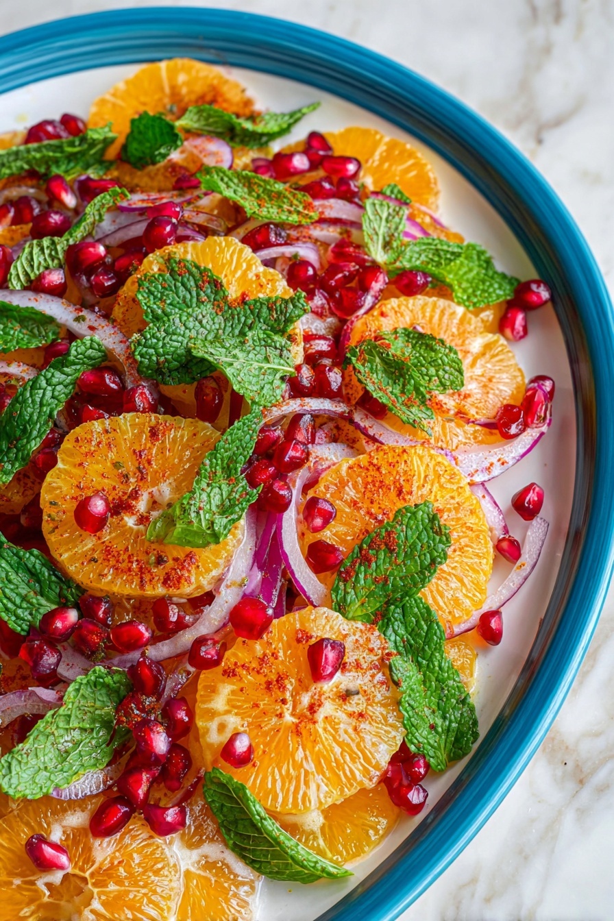 A white plate holds a colorful salad with four visible layers: the bottom layer is round, thin orange slices with a light dusting of red spice; the second layer consists of thin, pale purple onion slices scattered evenly; the third layer shows bright red pomegranate seeds spread across the dish, adding vibrant dots of color, and the final layer is fresh, torn green mint leaves placed on top and around the other ingredients. The contrast between the orange slices, red seeds, purple onion, and green leaves creates a lively and fresh look. The entire plate sits on a white marbled surface. Photo taken with an iphone --ar 2:3 --v 7