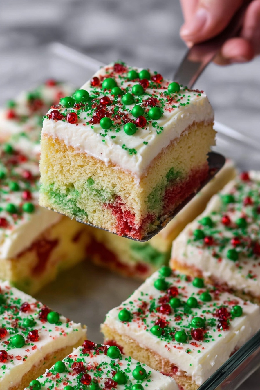 The image shows a slice of colorful sponge cake on a white plate. The cake has two main layers: the bottom layer is light yellow with sections of red and green sponge mixed inside, looking soft and airy with many small holes, while the top layer is white creamy frosting with a smooth texture. On top of the frosting, there are small round sprinkles in red and green colors evenly scattered. The background surface is a white marbled texture, and a red and white cloth is under the plate. Photo taken with an iphone --ar 2:3 --v 7