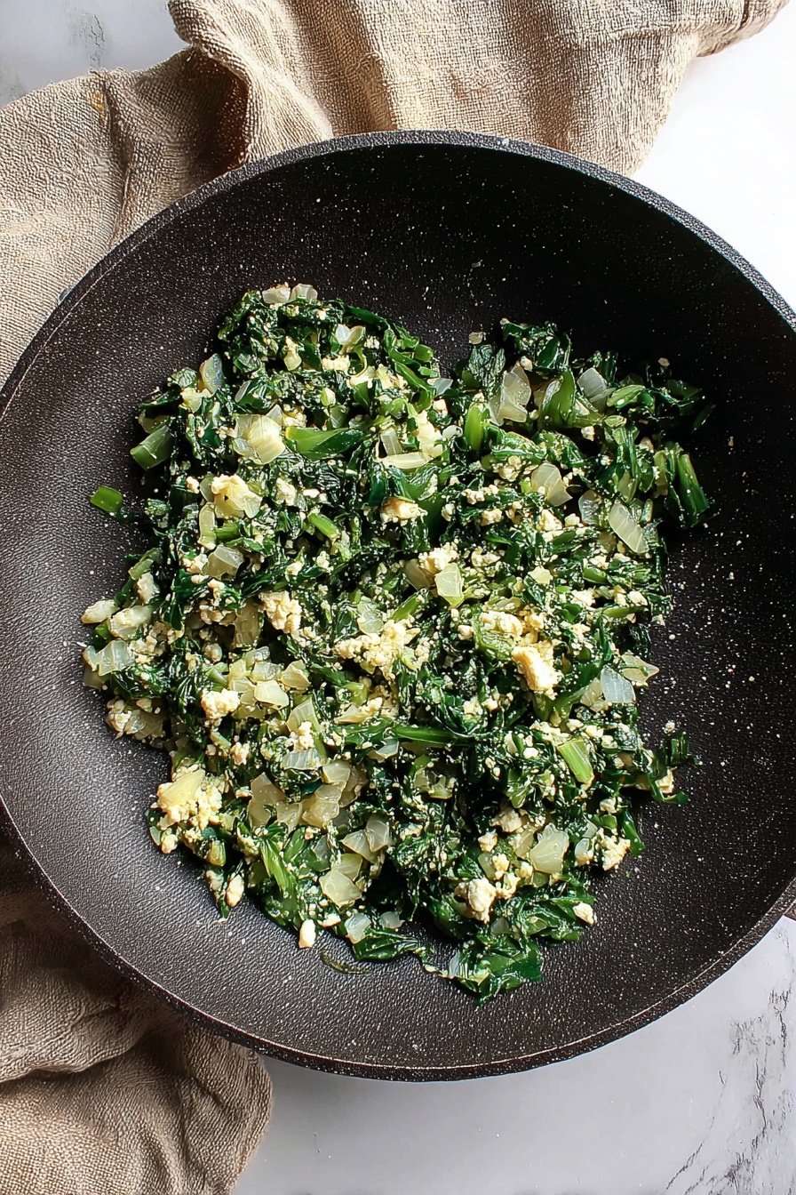 Four rolled crepes lie side by side on a white marbled surface, each filled with a mix of chopped cooked spinach and melted cheese visible at the open ends. The crepes have a thin, golden-brown outer layer with a slightly crispy texture on some edges. On top of one crepe rests two fresh green spinach leaves. Scattered around the crepes are small white cheese crumbles placed randomly on the surface. The bottom edge of the image shows a light gray textured cloth with frayed edges. Photo taken with an iphone --ar 2:3 --v 7